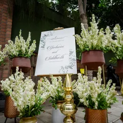 An elegant welcome setup featuring a personalized sign surrounded by fragrant tuberoses in earthy terracotta pots. The combination of rustic and refined elements creates a warm greeting.