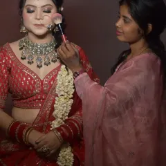 Another student gets hands-on experience creating a classic red bridal look. Notice her focus as she applies blush, a crucial step in balancing a bold lip and heavy eye makeup.