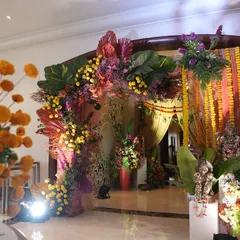 A grand and colorful entrance for a traditional wedding event. A lush arch of marigolds, purple blooms, and tropical leaves welcomes guests, flanked by statues and hanging floral strings, creating a festive and opulent first impression.