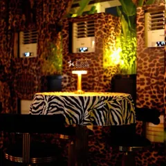 A cozy, intimate seating area within the 'Gilded Instinct' theme, featuring leopard-print walls and a zebra-print tablecloth.