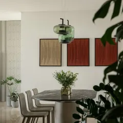 The dining area at Embassy Lake Terraces is anchored by a stunning marble-topped table and handblown green glass pendant lights. These elements work together to define the space, creating an intimate setting for meals that is complemented by the earthy tones of the wall art.