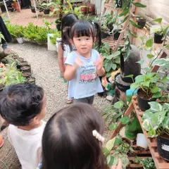 A child claps her hands with excitement during our visit to the nursery, surrounded by lush greenery.