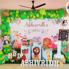 A vibrant jungle theme for a "Wild One" first birthday. This setup is packed with details, including a full balloon arch in shades of green, animal cutouts, themed plinths, and a large light-up number '1'.