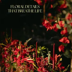 A close-up of the moody and romantic florals from the red Sangeet. The deep red flowers and taper candles create a sense of passion and drama, with the text "Floral Details That Breathe Life".