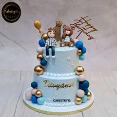 A royal teddy bear celebration cake for a first birthday. This 3kg two-tier chocolate cake features a fondant boy and teddy topper, decorated in a handsome blue and gold color scheme.