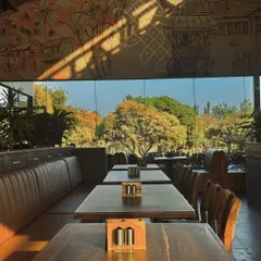 The restaurant's interior is designed to connect with its cultural context. A large, hand-painted mural depicting local village life runs along the wall, while the expansive glass windows frame the beautiful trees outside, creating a dialogue between art, nature, and design.