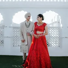 A regal couple portrait captured at a palace venue in Jaipur. The bride's vibrant red lehenga contrasts beautifully with the groom's elegant ivory sherwani, embodying the essence of a modern royal wedding.