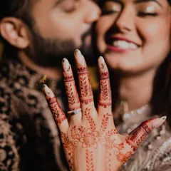 The moment after "yes". This beautiful shot focuses on her hand, adorned with intricate henna and the sparkling engagement ring, while the happy couple shares a kiss in the background.