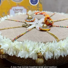 Celebrate the sweetness of Sawan with this handcrafted rafia box. Adorned with delicate white flowers and gota work, it's the perfect traditional packaging for ghevar or other mithai.