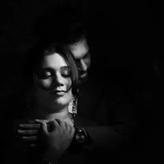 A dark and moody black and white portrait capturing a tender embrace. The focus is on the feeling of safety and love, with the shadows adding a sense of intimacy and privacy.