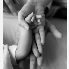 A baby's hand wrapped around their parent's finger. This macro shot in black and white emphasizes the delicacy of their tiny fingers and the strength of the bond.