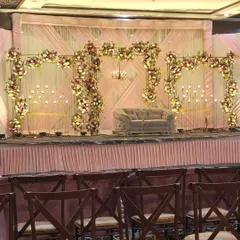 This wide shot shows a complete reception stage design before the event. The structure includes a metal framework adorned with flowers, a soft grey couple's sofa, and candle-like lighting against a draped backdrop.