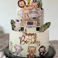 A super cute two-tier jungle safari cake for a first birthday. This cake is covered in adorable cartoon animals like a lion, giraffe, zebra, and monkey, ready for a wild celebration.