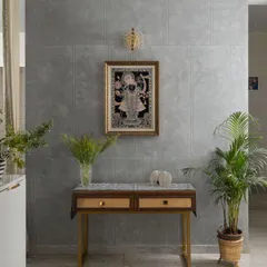 A tranquil corner featuring a traditional Pichwai painting against a modern concrete-finish wall. The simple console table with cane drawers creates a beautiful blend of contemporary design and Indian artistry.