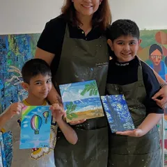 A mother and her two sons proudly show the paintings they created together during a family art session. Our studio is a welcoming space for artists of all ages.