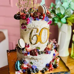 Berry tall, berry extra, berry delicious! This two-tiered cake for a 60th birthday is loaded with fresh berries, macarons, and edible flowers, all dusted with a touch of gold.