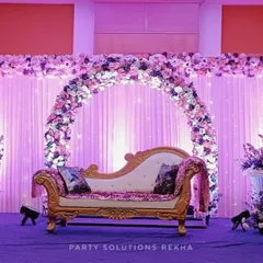 An elegant stage setup for a reception or engagement. The floral arch in shades of purple and white, combined with soft backlighting and a classic chaise lounge, creates a romantic and sophisticated focal point.