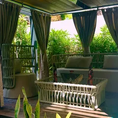 A close-up view of the pergola's interior, showing the comfortable daybed and unique woven chairs. The design details create a feeling of being in a high-end resort.
