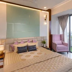 This luxurious bedroom features a pastel green accent wall with metallic inlay, paired with a comfortable pink wingback chair. The combination of soft colors and rich textures creates a chic and inviting retreat.