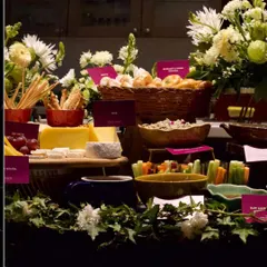 This abundant grazing table is woven with fresh flowers and greenery, blurring the line between food and decor. It features a variety of cheeses, dips, breads, and crudités, all artfully arranged to invite exploration.
