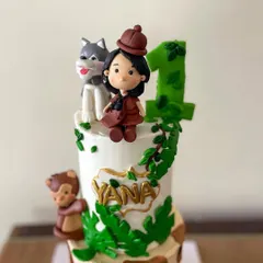 A jungle-themed two-tier cake for a first birthday celebration. The design features a giraffe print bottom tier, a vine-covered top tier, and adorable handmade fondant animals like a monkey, leopard, donkey, and a husky.