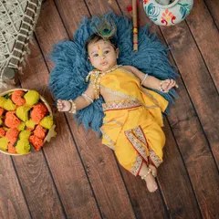 An overhead shot of a baby dressed as Krishna, lying on a soft blue rug. This angle provides a unique perspective and highlights the intricate details of the costume and props.