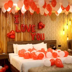A sweet and simple romantic room setup. This decoration includes 'I Love You' foil balloons, red and white balloons on the bed and ceiling, and warm ambient lighting.