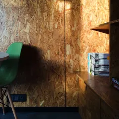 An interior detail of the journalist's workspace, showing the rich texture of the OSB walls and the simple, functional built-in shelving. The design is minimalist yet highly practical.