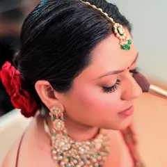 A close-up of the bride's getting-ready process, focusing on the final touches of makeup. The red rose in her hair adds a beautiful, classic detail.