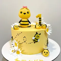 A bee-utiful cake for a first birthday! This sweet design features a bright yellow buttercream finish, fondant daisies, and adorable little bees, including a custom Cocomelon-style bee topper.