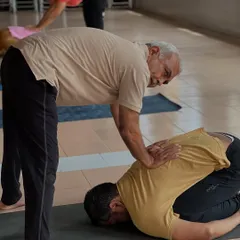 An elder teacher offers guidance in Child's Pose. The wisdom of experience is passed down through careful, compassionate correction.
