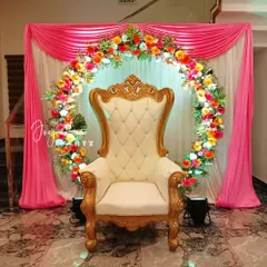 A beautiful floral ring backdrop perfect for a half saree function at home. We use a mix of colorful flowers to create the ring, complemented by elegant pink drapes and a classic throne chair.