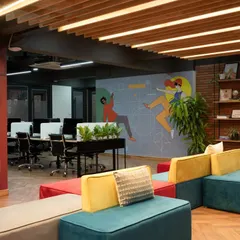 A wide view of the main huddle space, featuring the iconic red phone booth, colorful seating, and a large wall mural. This area is the social and collaborative heart of the office.