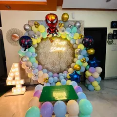 A fun Spiderman theme for a 4th birthday. This setup features a circular balloon arch in pastel colors, Spiderman foil balloons, a neon sign, and a light-up number '4'.