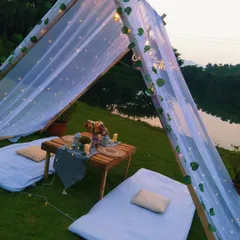 A side view of the lakeside tent, showcasing the delicate drapery, leaf garlands, and the serene natural surroundings. We can set up these custom experiences at farmhouses or private villas in places like Karjat.
