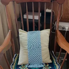 Here is the same blue tie-back shown on a cushion placed in a classic wooden rocking chair. It demonstrates how these accessories can add a touch of personalized, cozy charm to any seating area in your home.