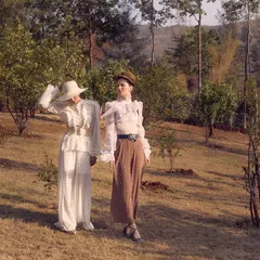A wider shot from the Starchthelabel campaign, showing two models in a pastoral landscape. The styling contrasts an all-white vintage look with an earth-toned ensemble, creating a beautiful visual dialogue that enhances the collection's romantic narrative.