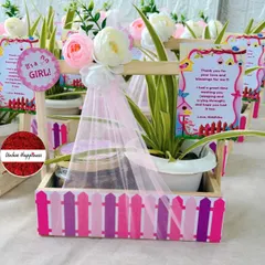 A charming "It's a Girl!" announcement favor, featuring a pink picket fence design, a live plant, and a jar of cookies, complete with a sweet thank you note.