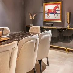 A luxurious dining room setting with a dark marble table and cream-colored upholstered chairs. The scene is completed by a high-gloss black sideboard with gold accents, creating a sophisticated space for formal entertaining.