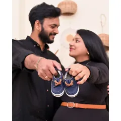 This is such a classic and sweet maternity pose. The couple holds up a tiny pair of baby shoes, a symbol of the little one they are so excited to meet. The Boho decor in the background adds a warm, stylish touch.