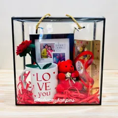 This Valentine's hamper comes in a modern acrylic tote bag. It's filled with a "Love You" mug, a personalized photo frame, a handmade crochet rose, a teddy, and Ferrero Rochers.