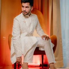 A regal portrait of the groom, Noman, seated in a classic chair. The warm lighting and his elegant sherwani create a picture of pure sophistication.