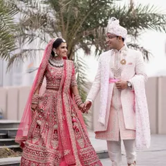 A candid shot of a newly married couple walking hand-in-hand, showcasing the bride's vibrant pink lehenga and the groom's elegant sherwani in a natural, outdoor setting.