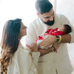 A new family of three, glowing with happiness. The parents look lovingly at each other while the father securely holds their newborn son.