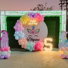 A magical unicorn-themed party for a 5th birthday. This outdoor setup features a pastel rainbow balloon arch, unicorn cutouts, a personalized backdrop, and a light-up number '5'.