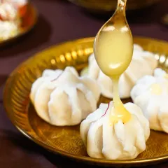 A delicate pour of warm ghee over beautifully crafted modaks, a sweet dumpling central to Maharashtrian festivals. The action shot emphasizes the richness and tradition of this beloved dessert.