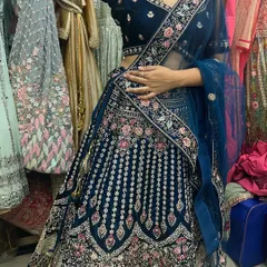 A customer trying on a stunning navy blue velvet lehenga with intricate pink and silver floral embroidery. This is a perfect choice for a winter wedding reception.