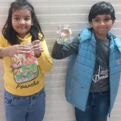 Two proud students showing off the garden-themed jars they decorated with clay. These workshops help develop fine motor skills and creativity.