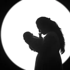A mother's silhouette, holding and gazing at her newborn baby. The backlighting creates a halo effect, emphasizing the sacredness of this first connection.