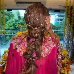 If spring had a hairstyle, this would be it! A close-up of the beautiful braided Mehendi look, showing the delicate star pins, pearls, and fresh pink flowers.